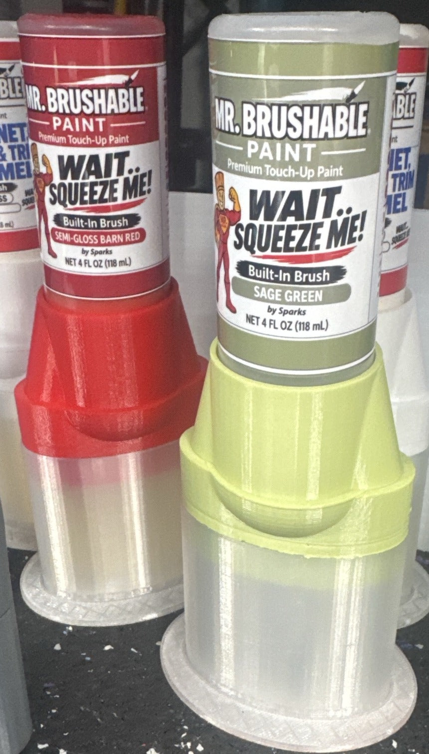 Mr. Brushable brush bottles in semi-gloss barn red and sage green, each labelled “Wait.. Squeeze Me!”, on a shelf